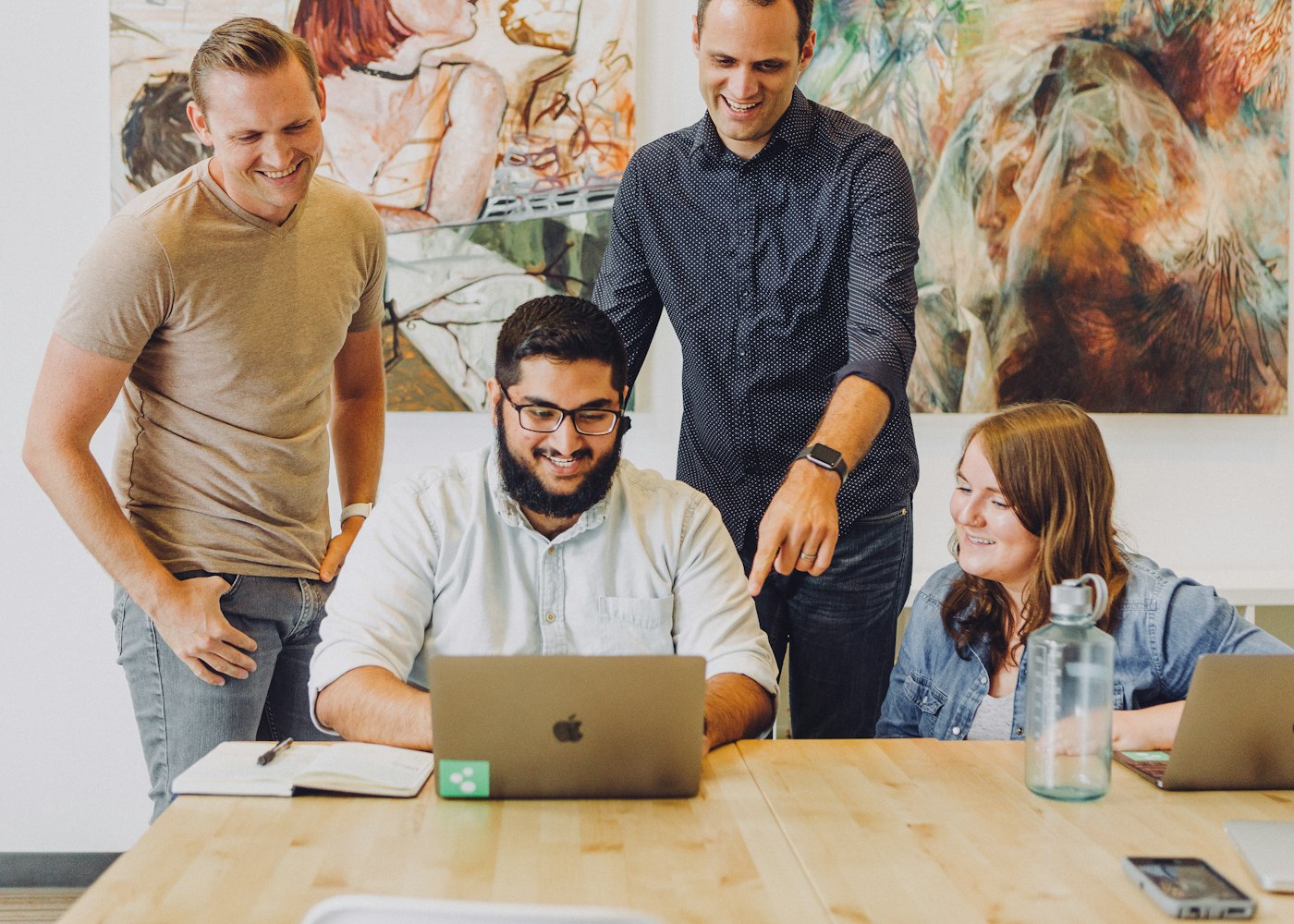 Four colleagues smiling and collaborating around a laptop